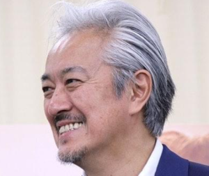 「穏やかな笑みを浮かべる声優・山路和弘さんの近影。白髪混じりの髪と整えられた髭が、彼が演じる老練な魔法使いデンケンの深みと重なるような、温かくも鋭い眼差しを感じさせる一枚。